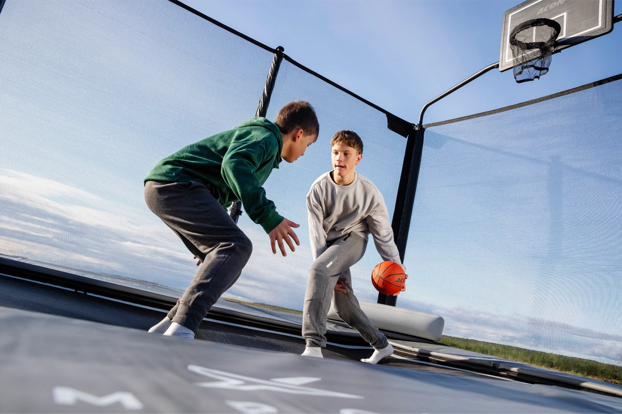 Two teenage kids playing basketball on an Acon X garden trampoline with a basketball hoop.