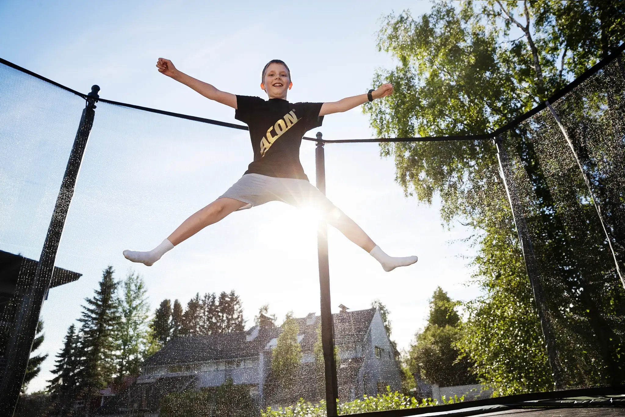 Young boy doing an X-jump on an Acon trampoline while wearing an Acon t-shirt.