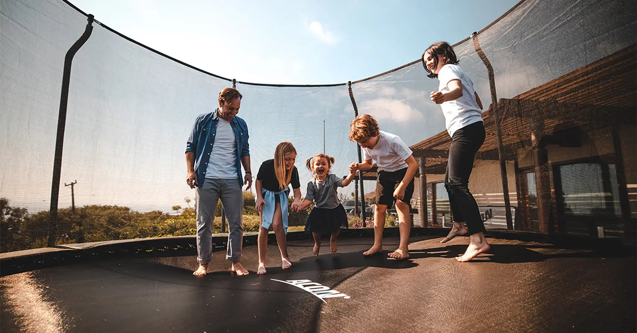 Happy family with parents and three kids jumping on a round Acon trampoline with safety net.