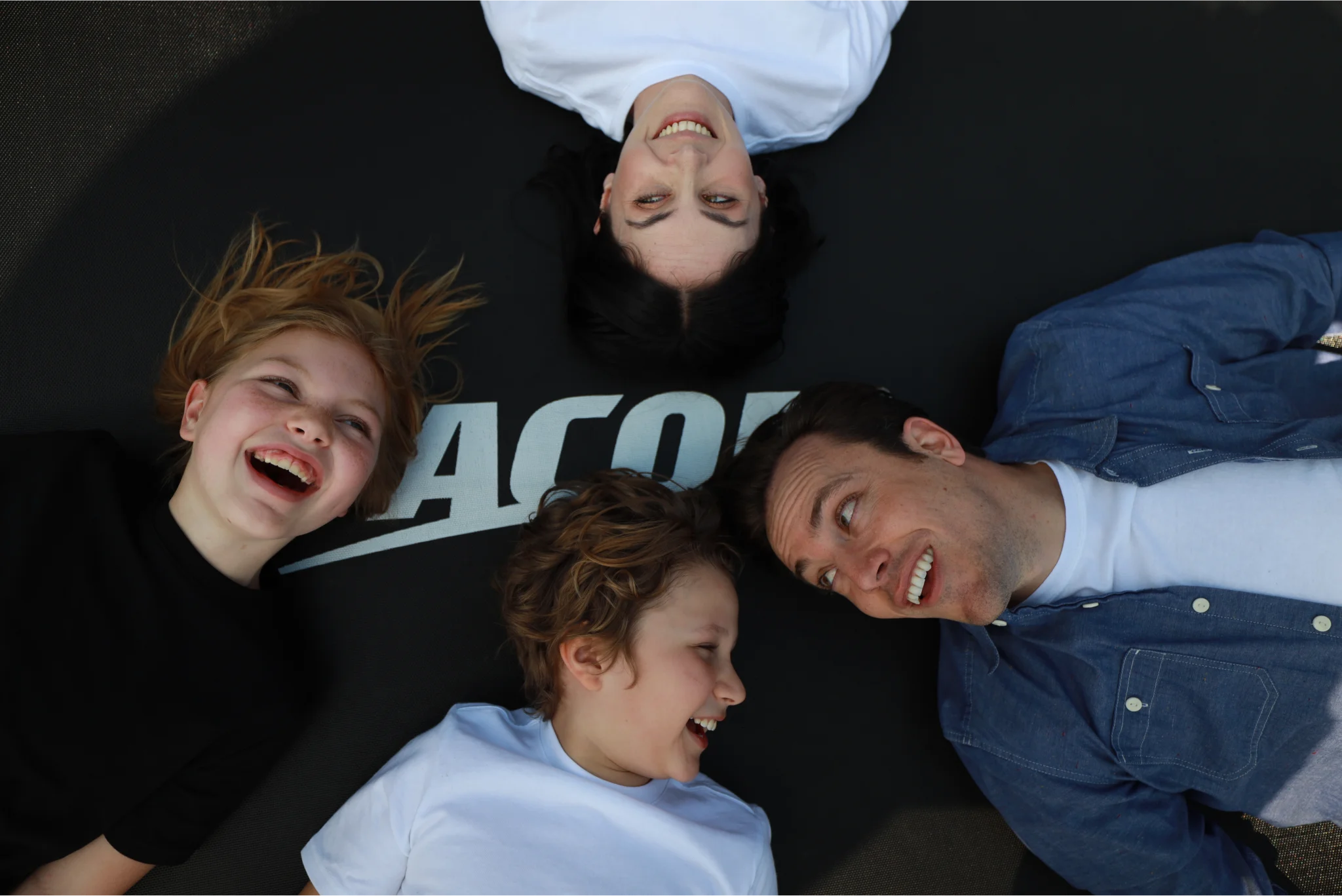 Smiling family with two kids laying on an Acon trampoline.