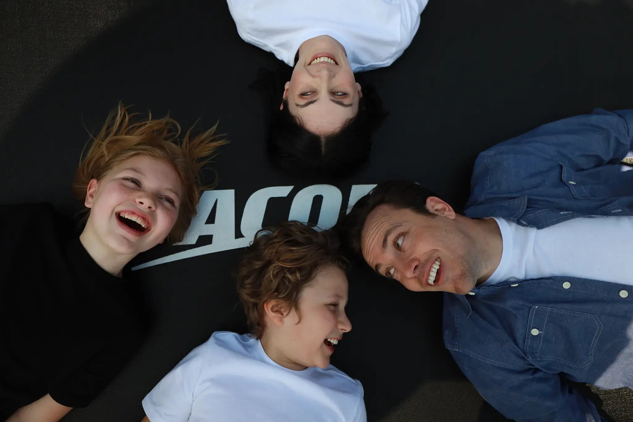 Close-up photo of a family of four smiling and lying on an Acon trampoline.