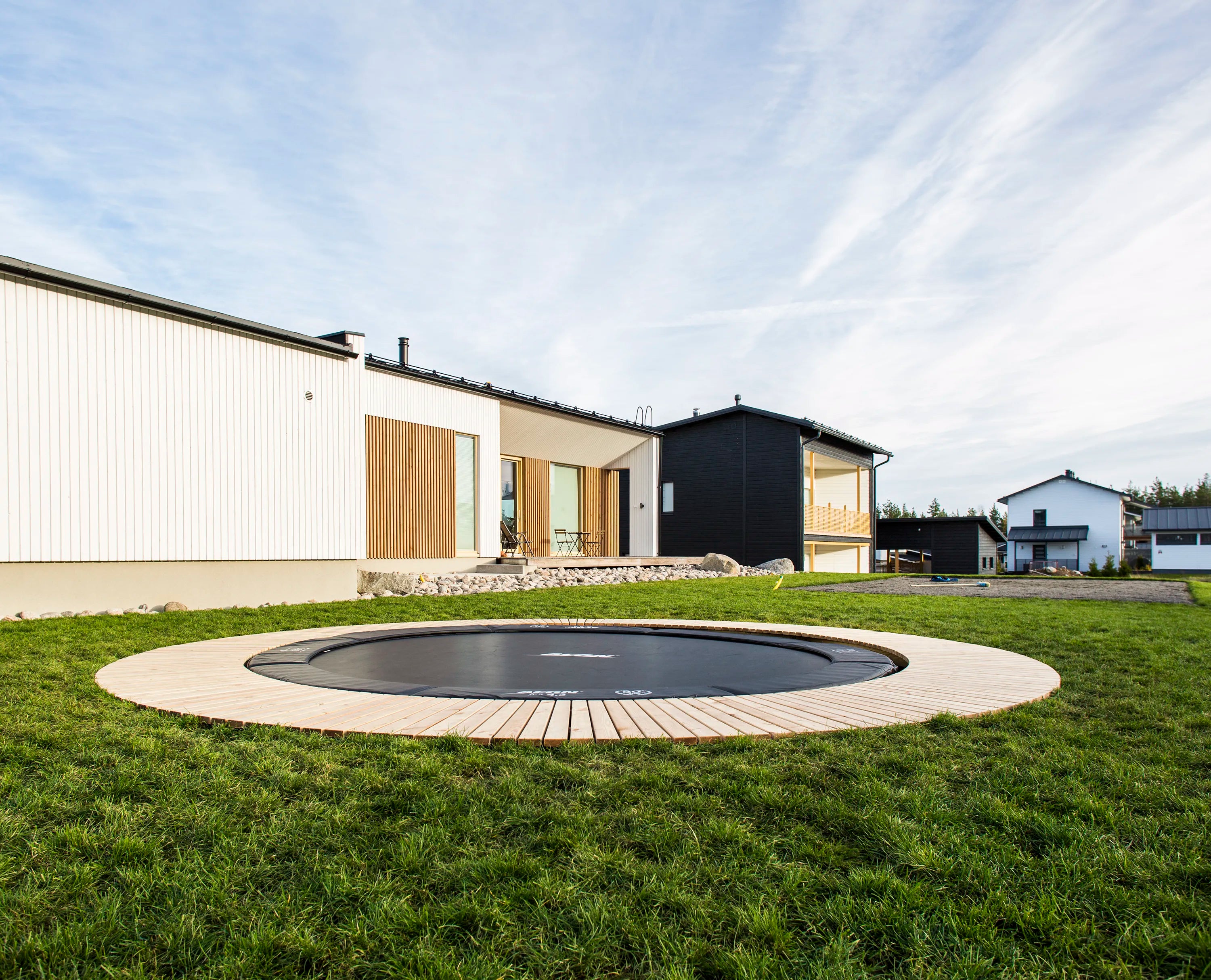 A round Acon trampoline installed in the ground. Surrounded by decorative wooden panels.