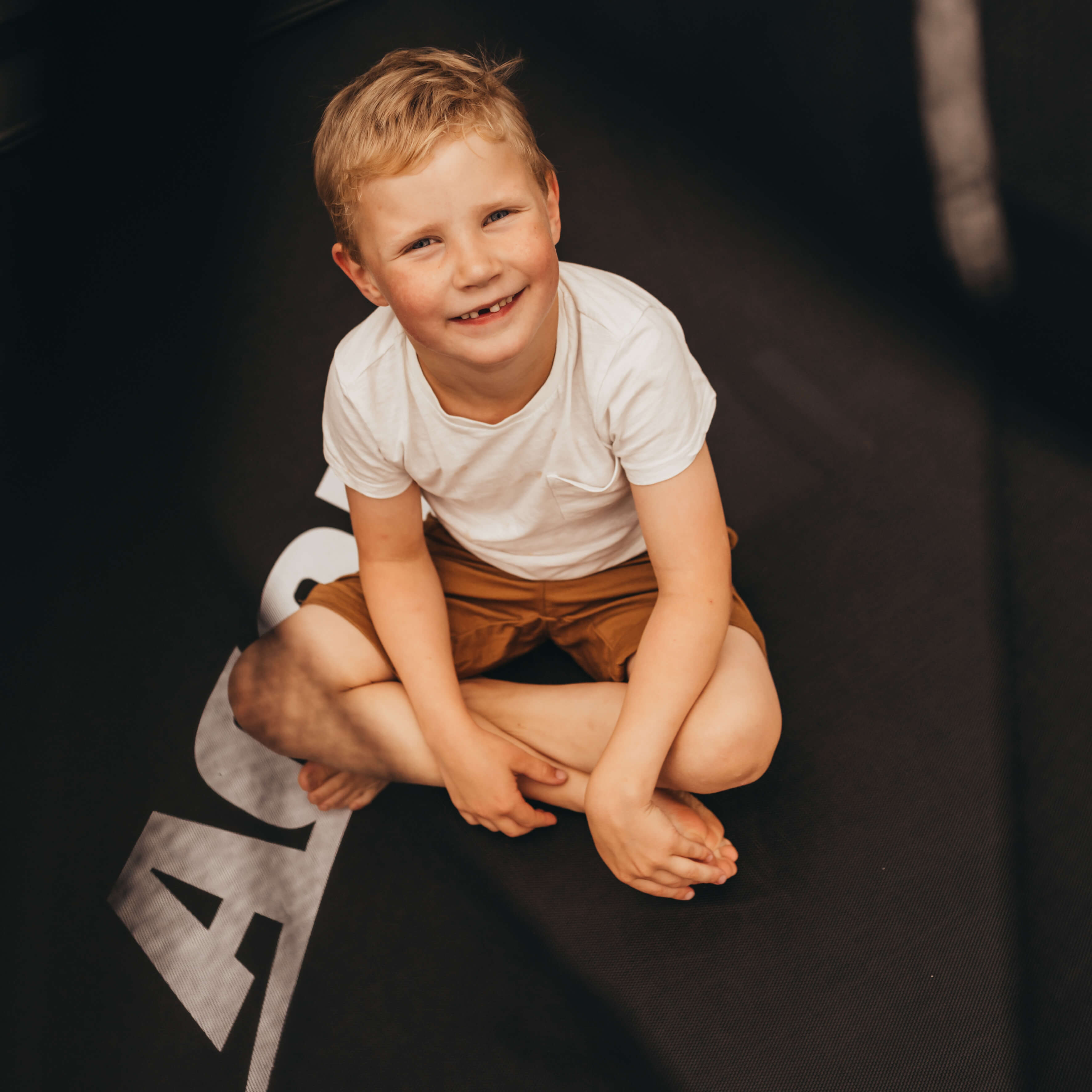 A laughing boy sits on an Acon trampoline.