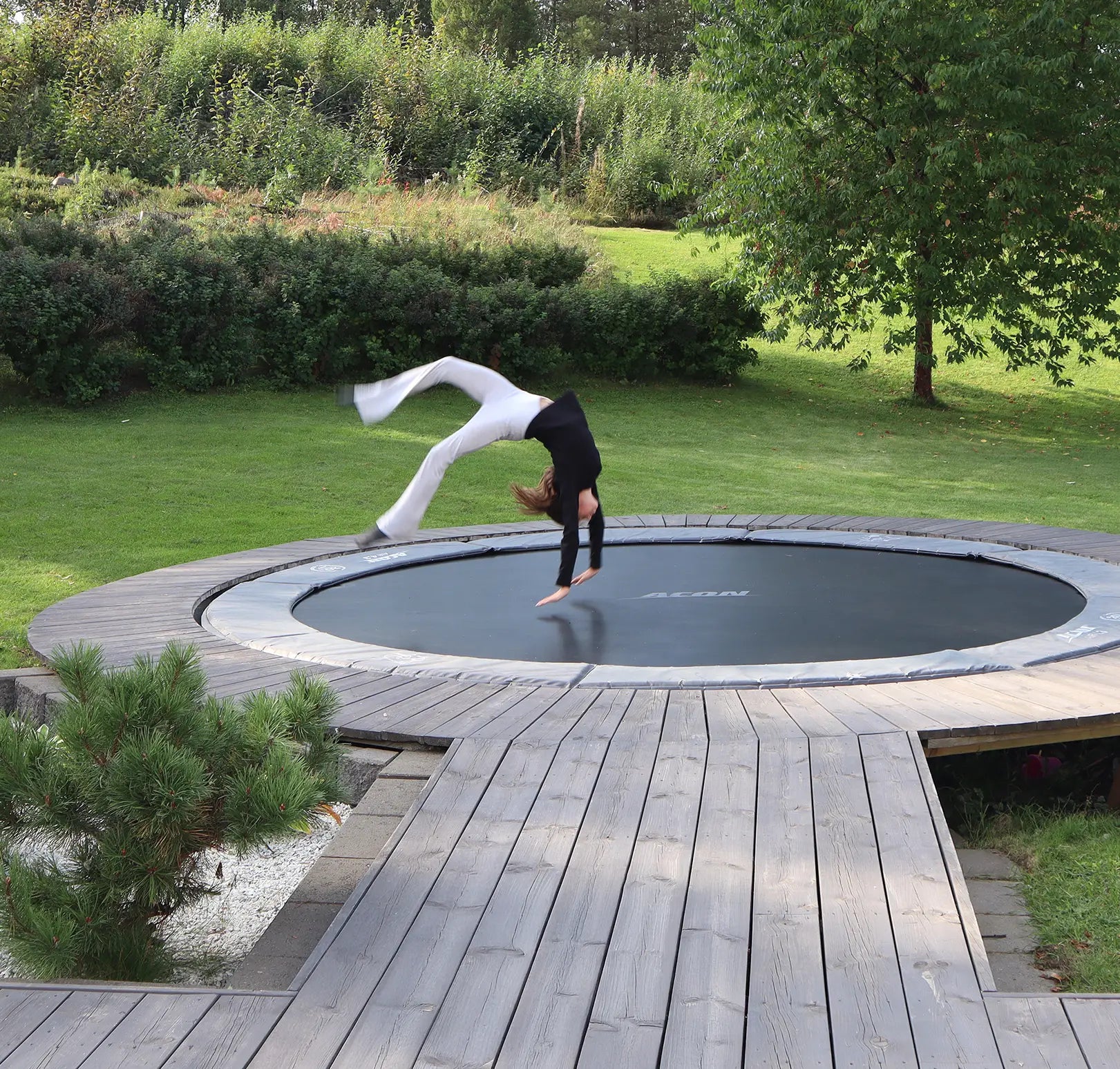 A girl jumping on a trampoline embedded in the terrace in the backyard.