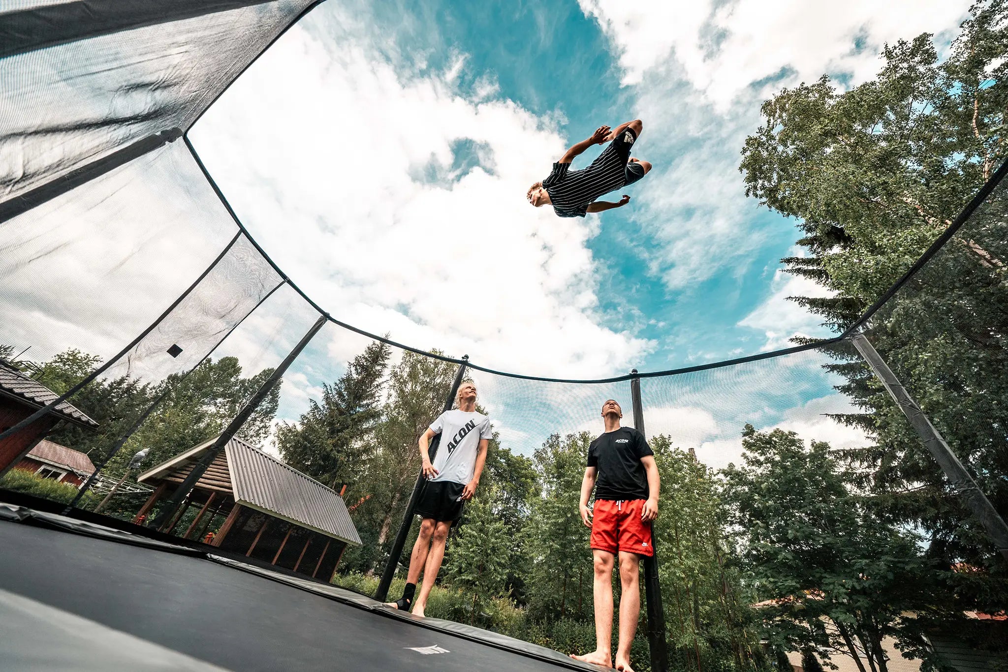 Three trampoline athletes on a Acon trampoline, one is jumping very high while other watch.