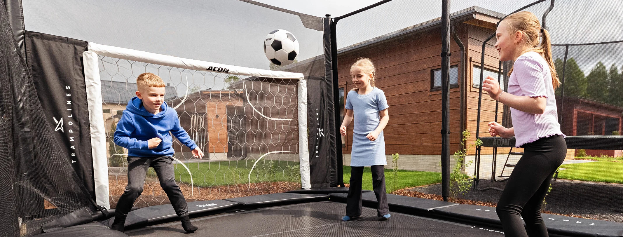 Children playing with a soccer ball on an Acon X 17ft trampoline with a soccer goal in the background.