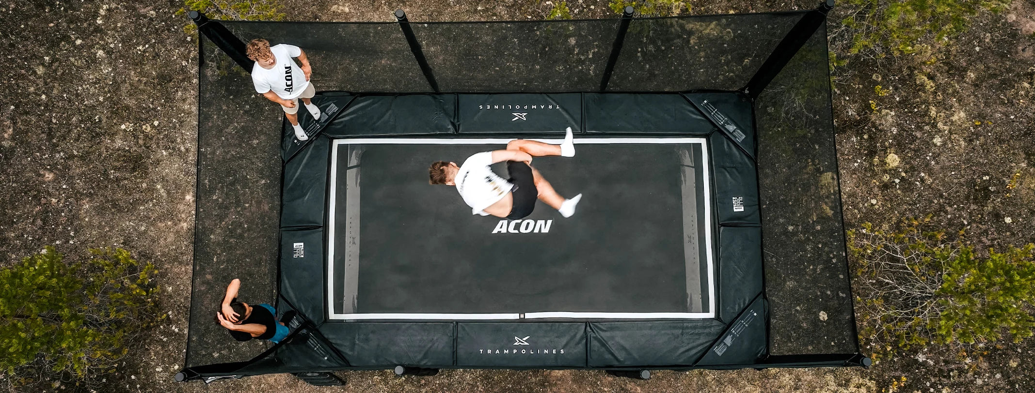 Three people tricking on an Acon X 17ft trampoline in an outdoor setting.