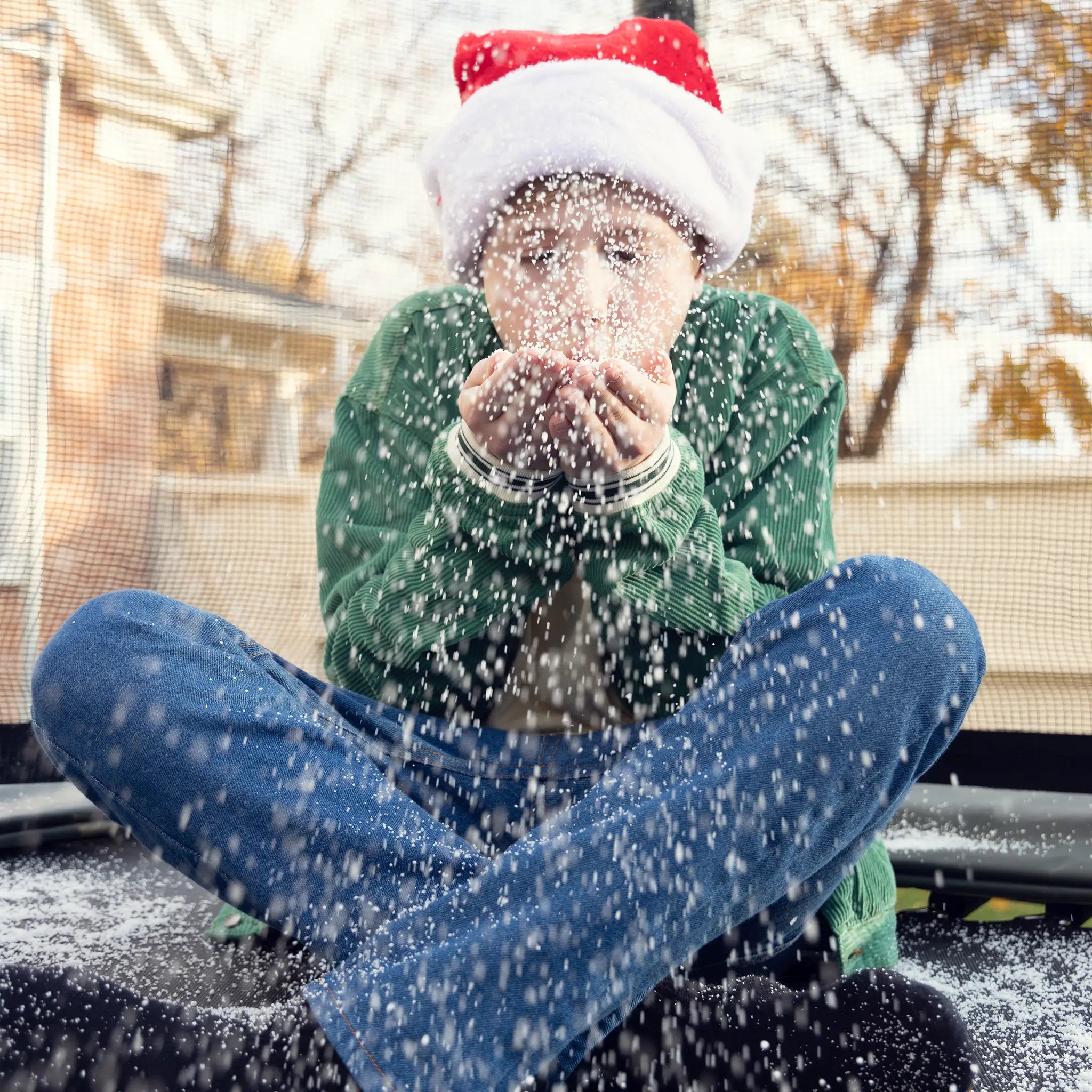 Child wearing a Santa hat blowing snow while sitting on a Acon trampoline.