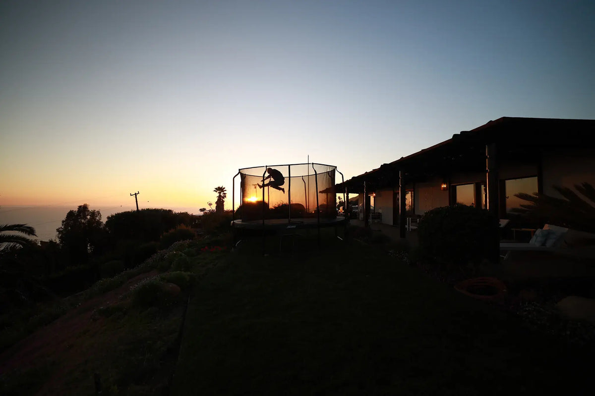 Child jumping on a backyard trampoline at sunset.
