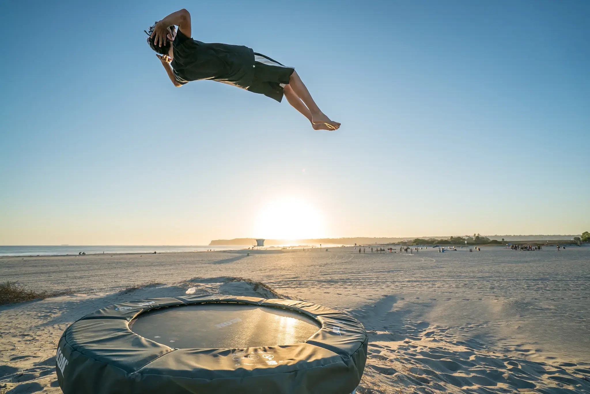 Boy jumping a flip on a small Acon trampoline at the beach.