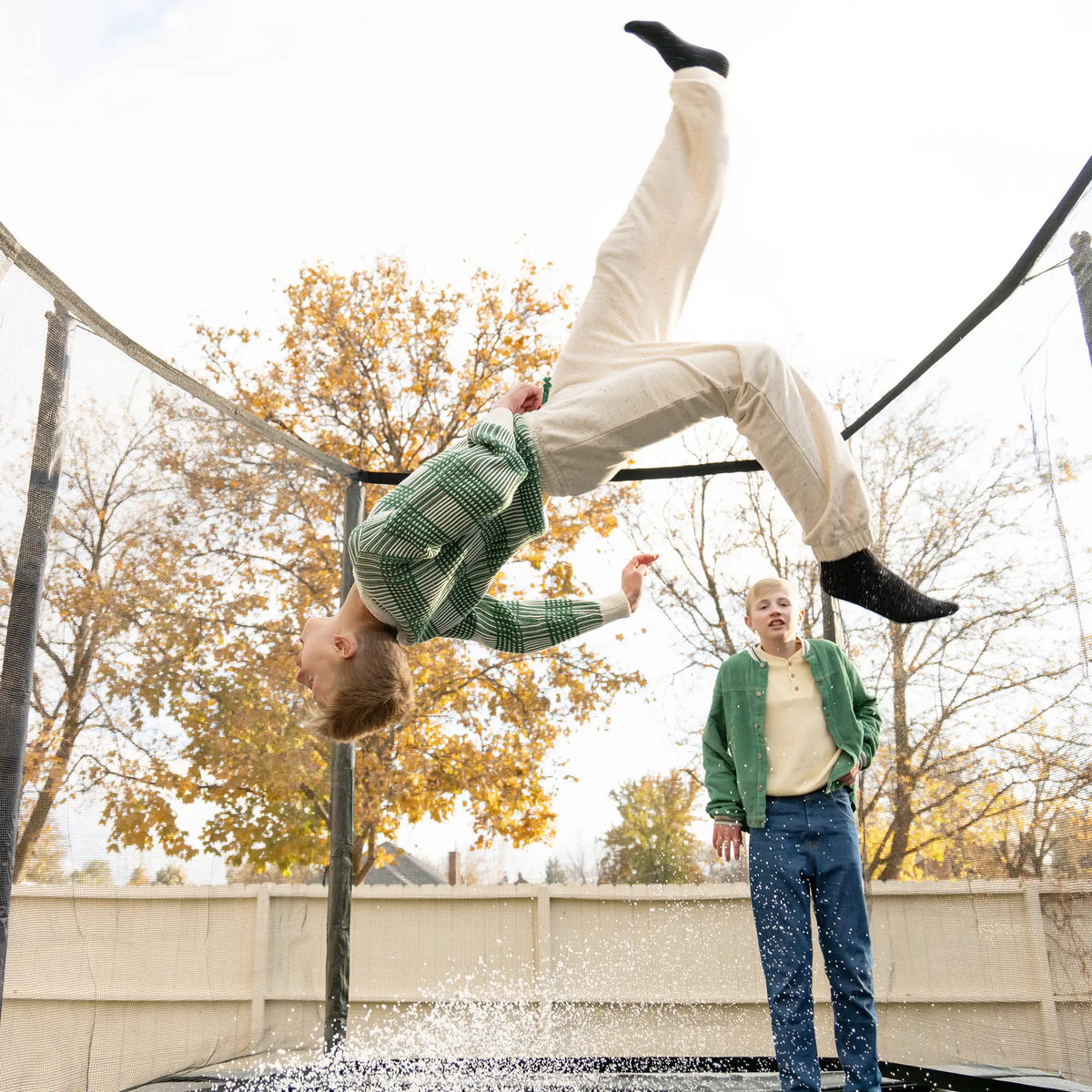 Two boys jumping on a Acon trampoline, one is doing tricks and the other one is watching.