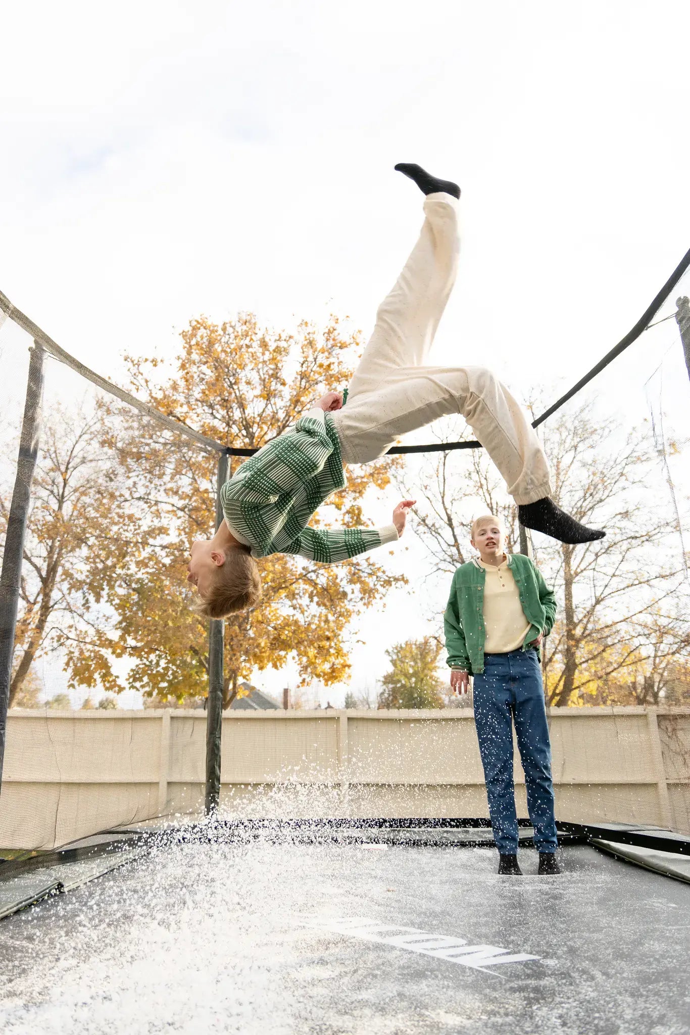 Two boys jumping on a Acon trampoline, one is doing tricks and the other one is watching. 