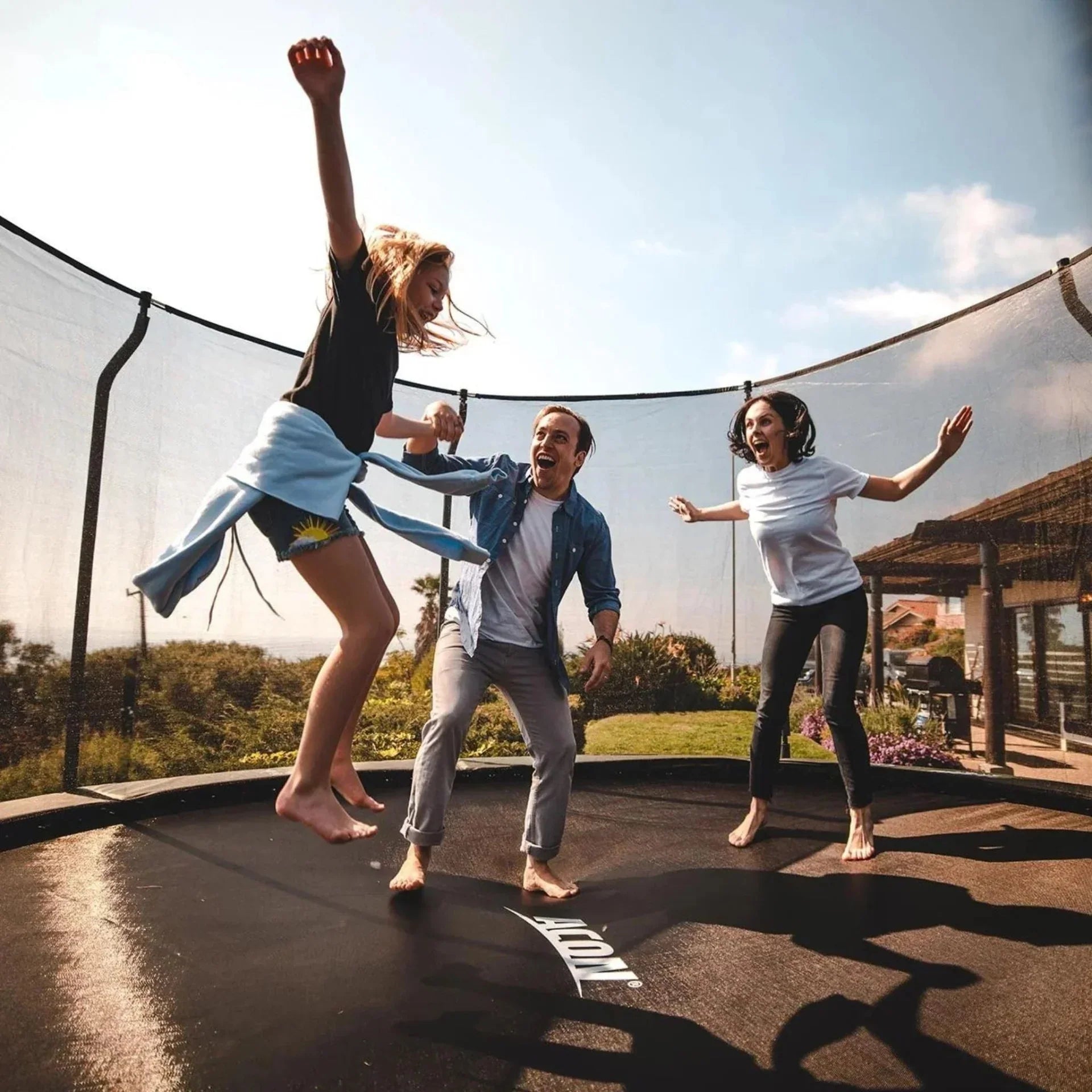 Family on an Acon trampoline, with a girl jumping and parents standing.