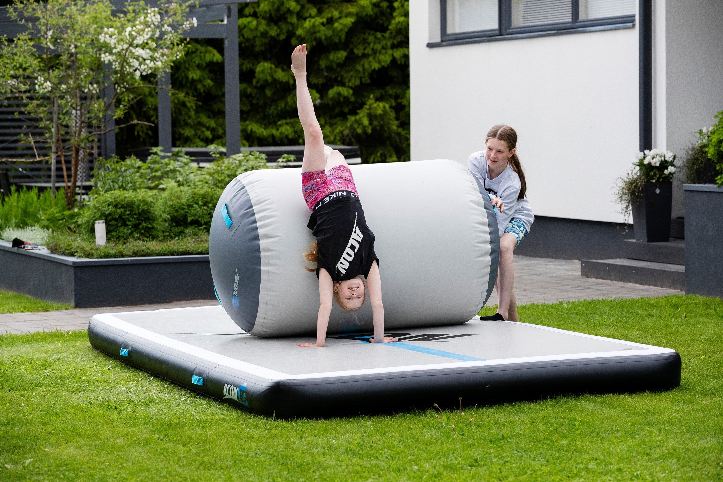 Two girls practicing flips with the help of Airroll and Airtrack in their backyard