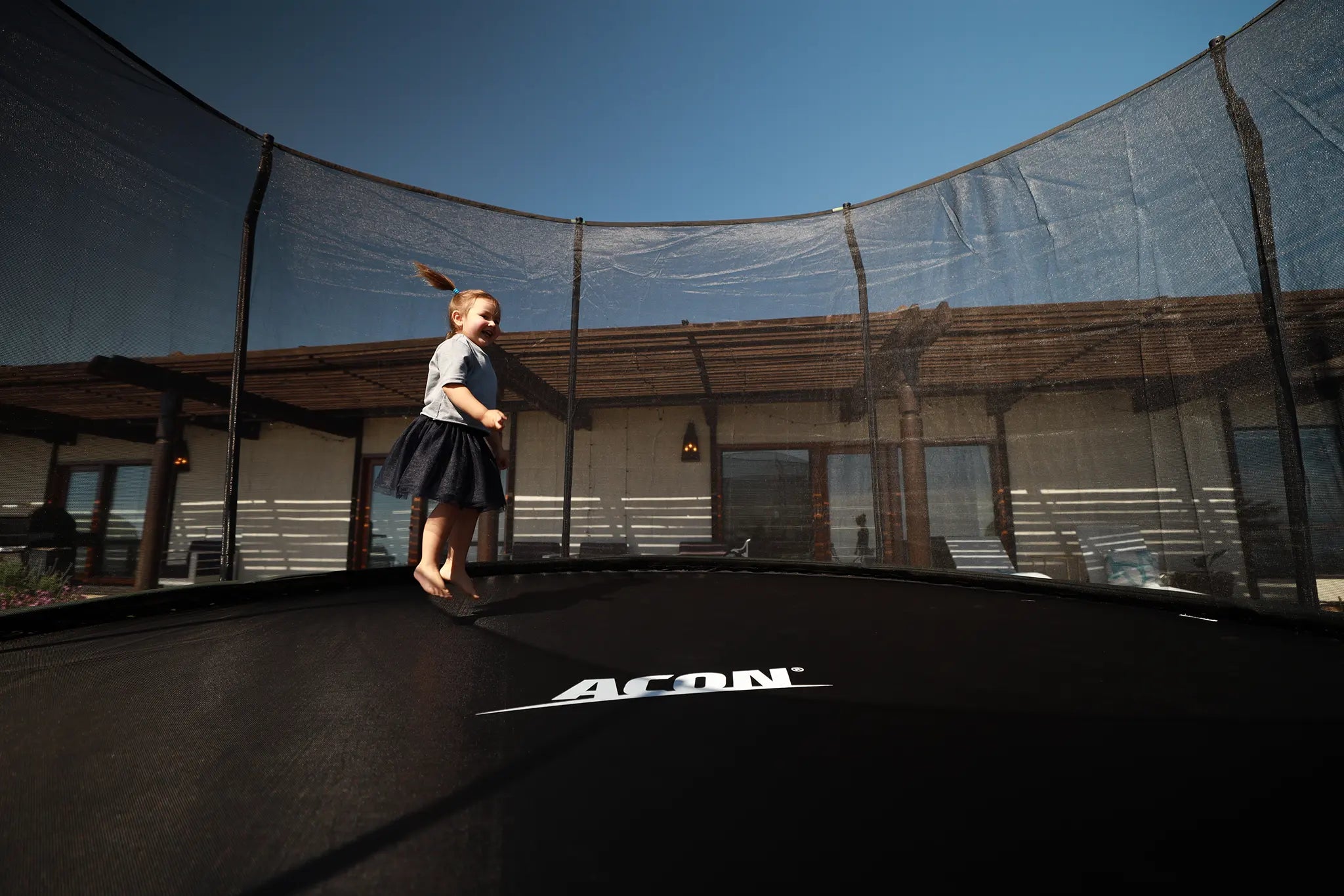 Youn girl jumping on a round Acon trampoline with safety net. 