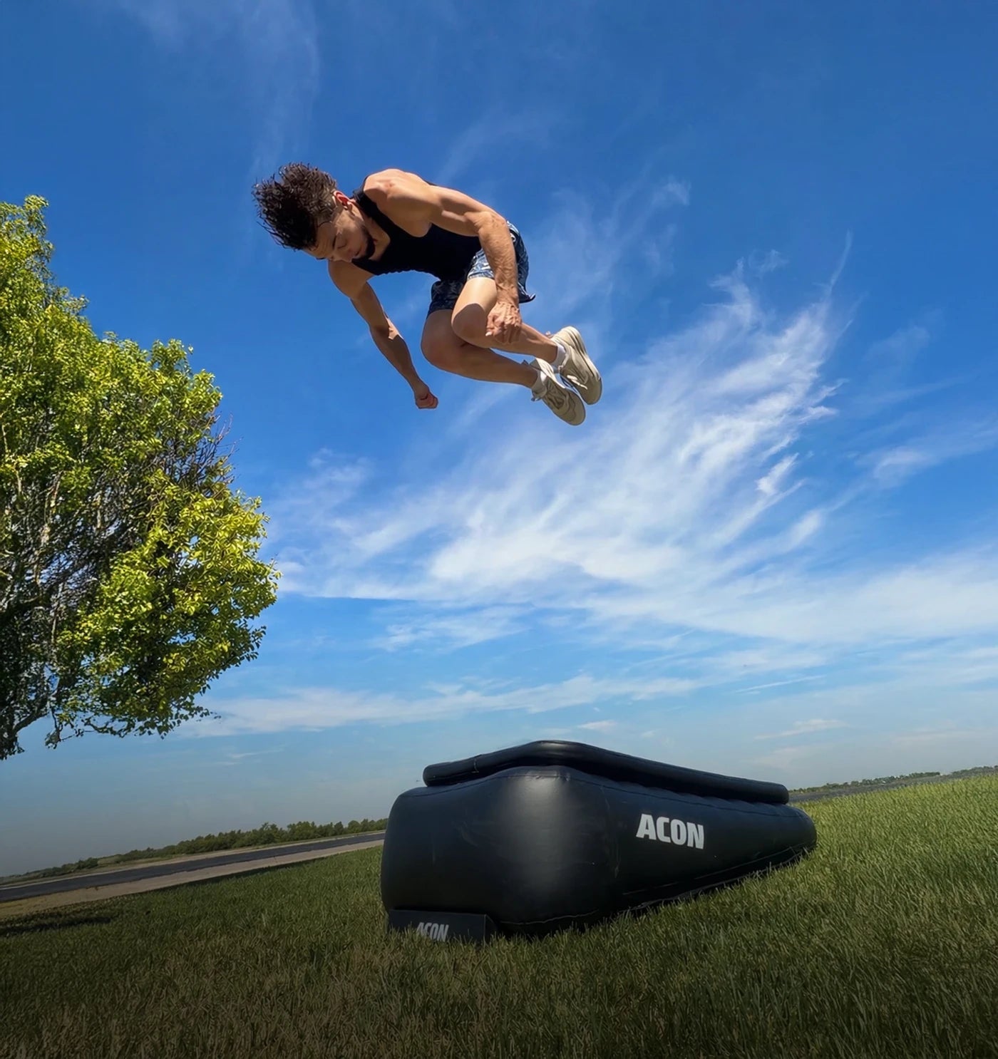 Man performing a high frontflip on an Acon Airboard outdoors, the Airboard on grass.
