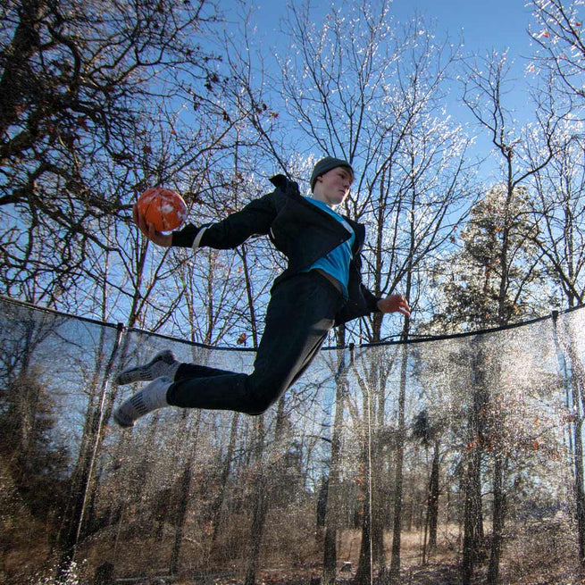 Boy jumping on ACON trampoline with basketball in hand
