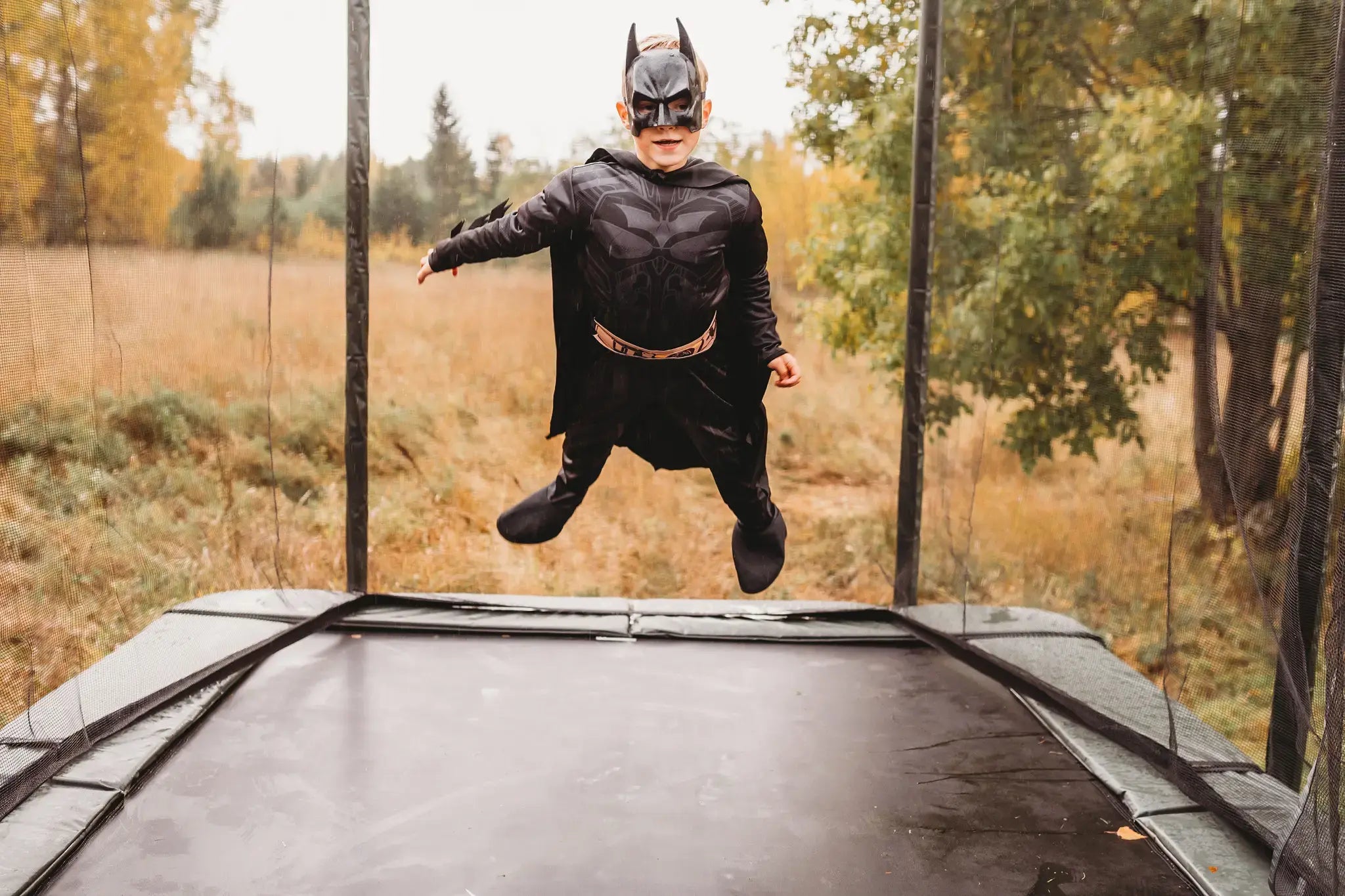 Young boy wearing a batman costume and jumping on an Acon trampoline. 
