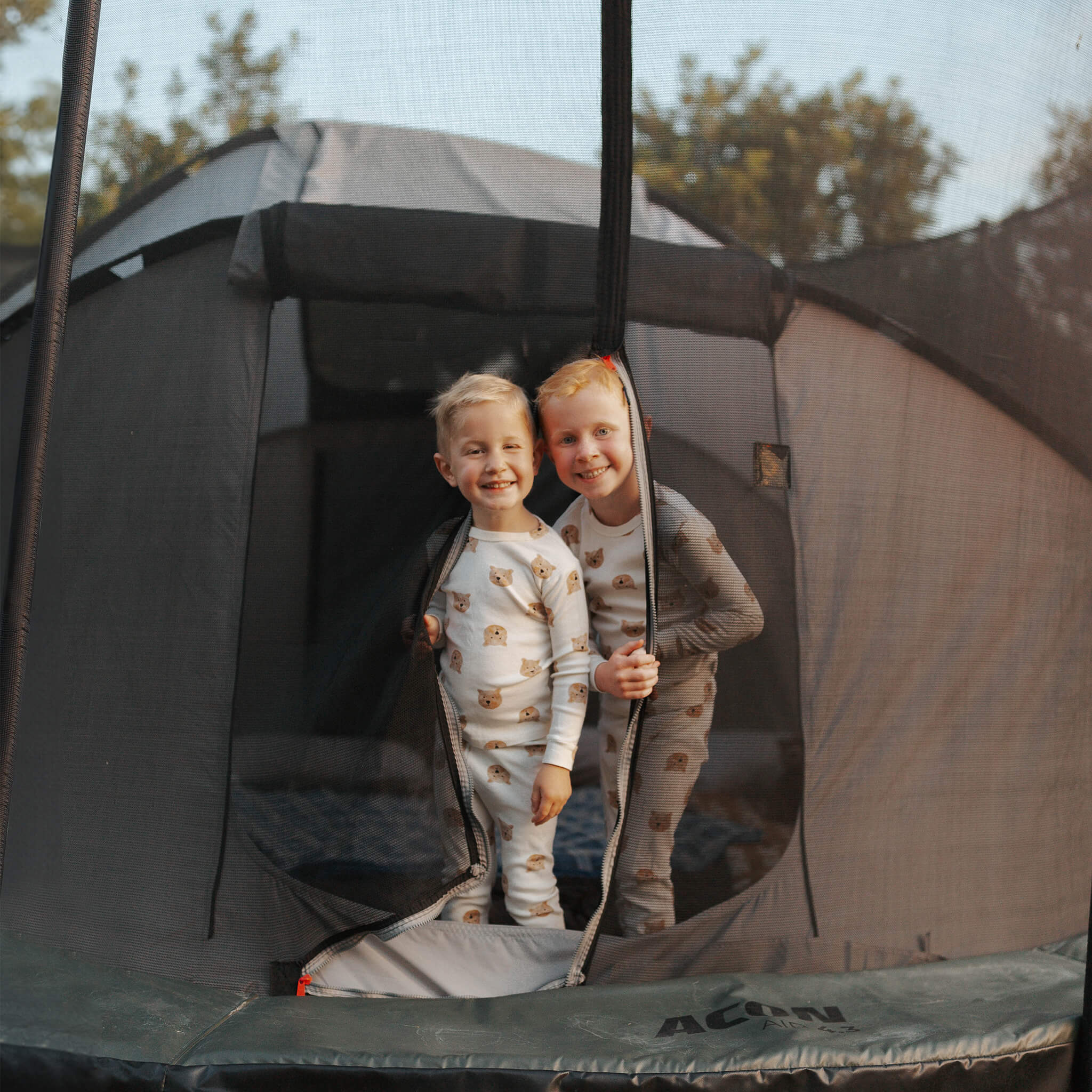 Two children are standing in the doorway of the Acon Trampoline Tent.