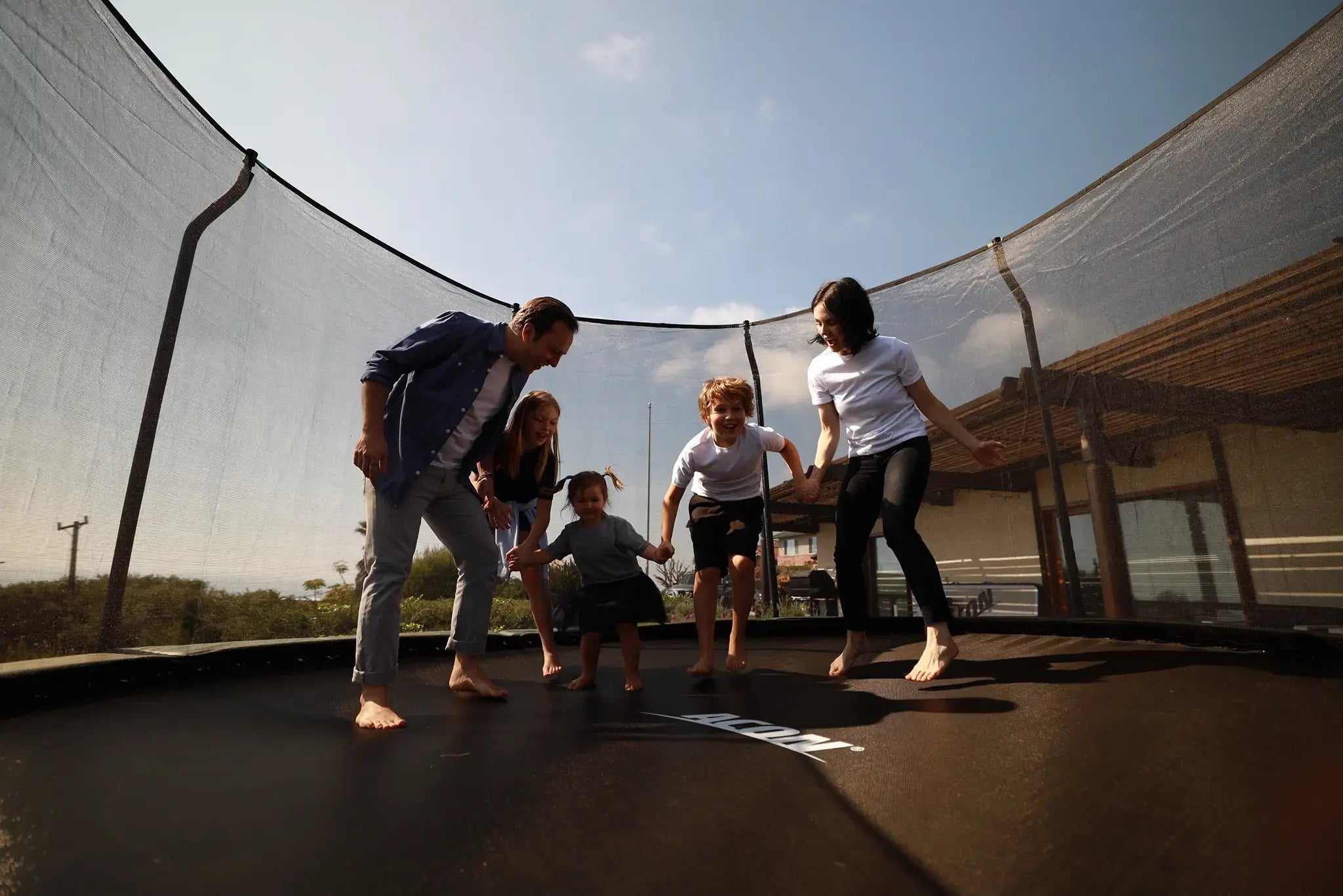 A family of five jumping and playing together on a Acon trampoline outdoors.