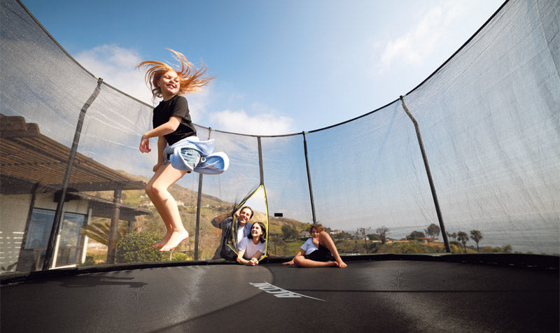 A family watching a little girl jumping on a trampoline with enclosure