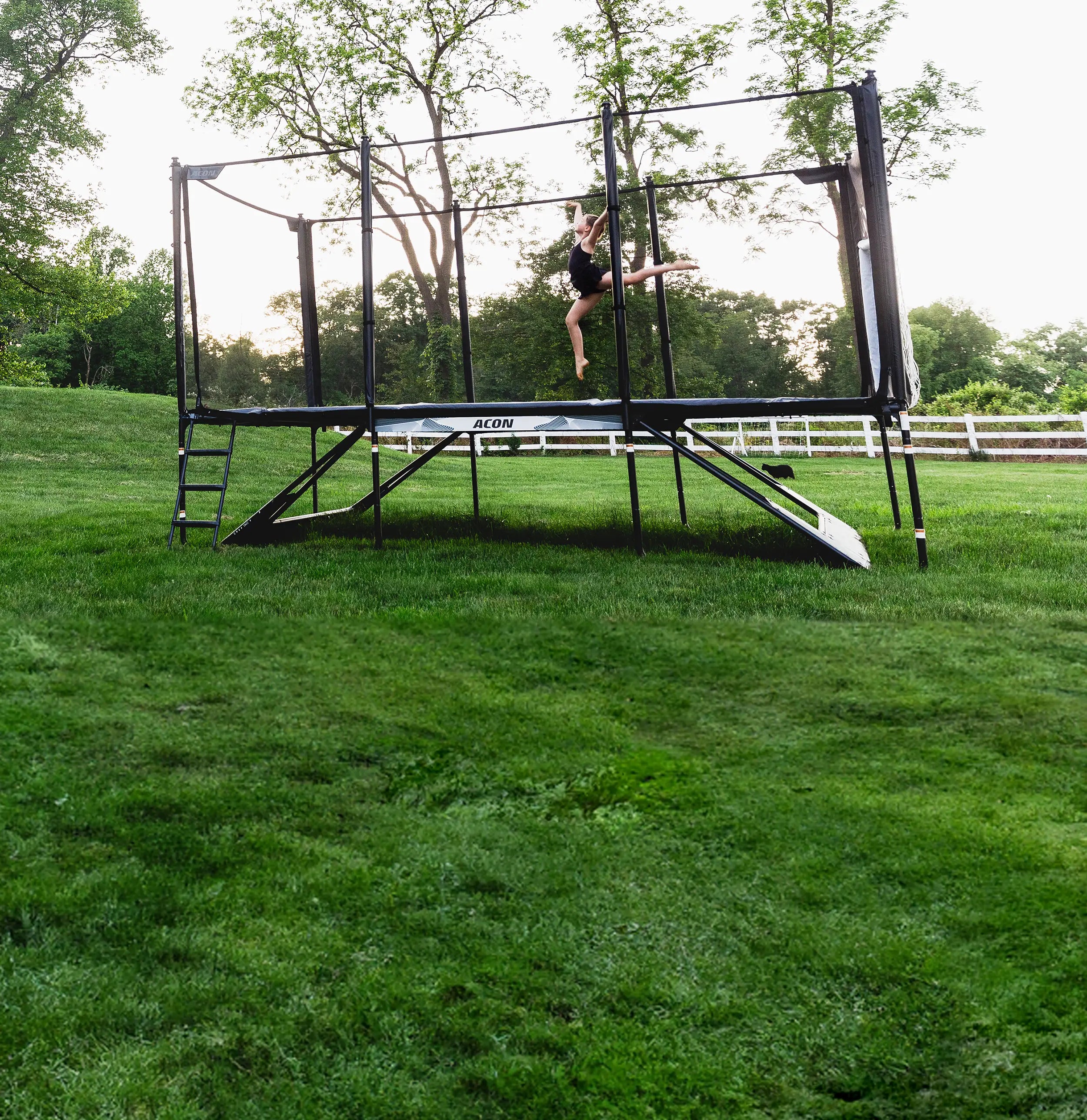 A girl is jumping on an Acon X trampoline, which is placed in a summery backyard.
