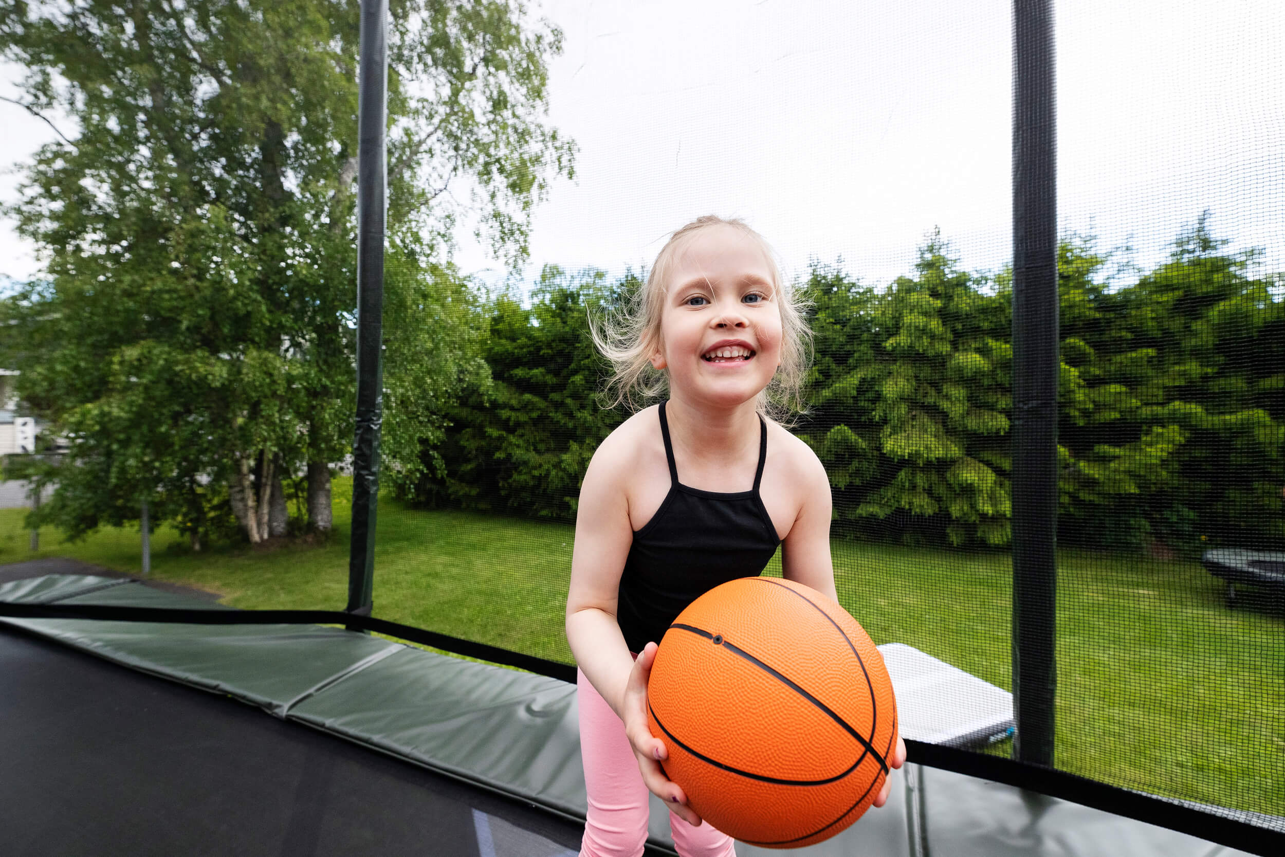 Happy girl on Acon trampoline holding a trampoline basketball.