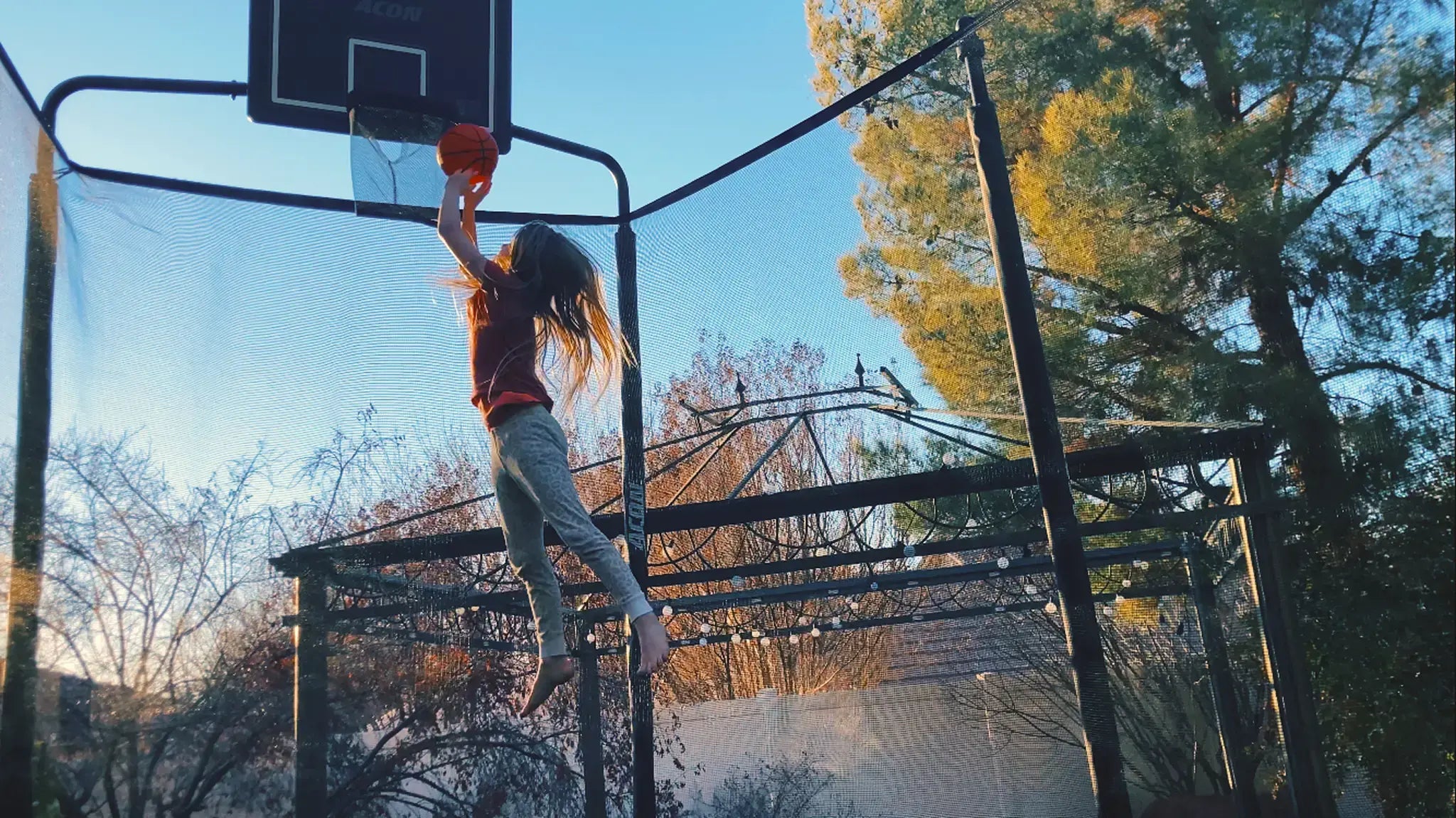 Young girl jumping on an Acon trampoline and playing basketball with Acon trampoline hoop. 