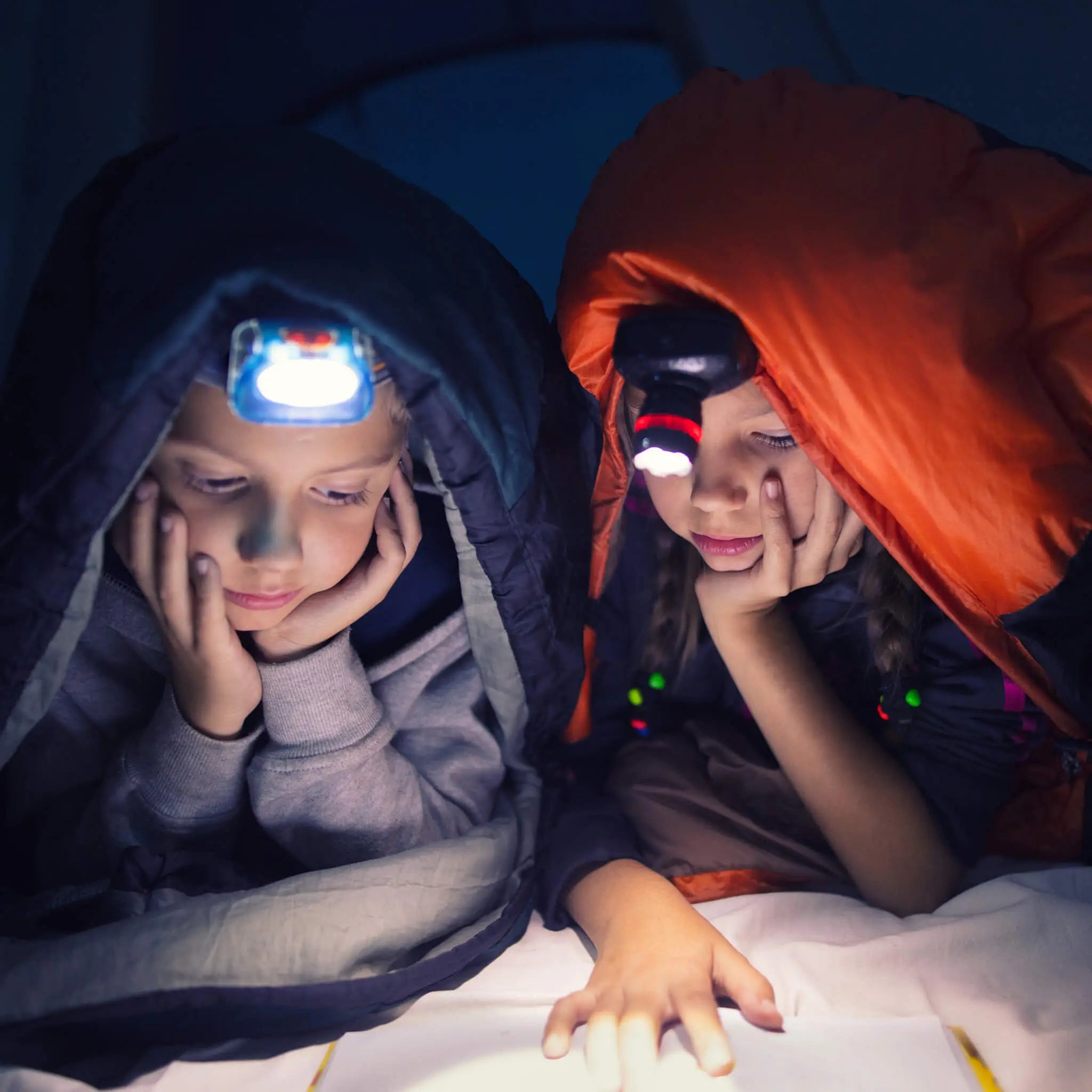 Girls wearing headlamps reading in a tent.