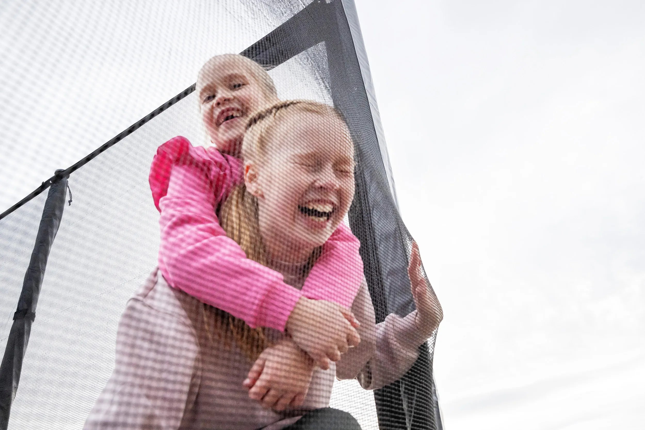 Two laughing girls behind a trampoline safety net.