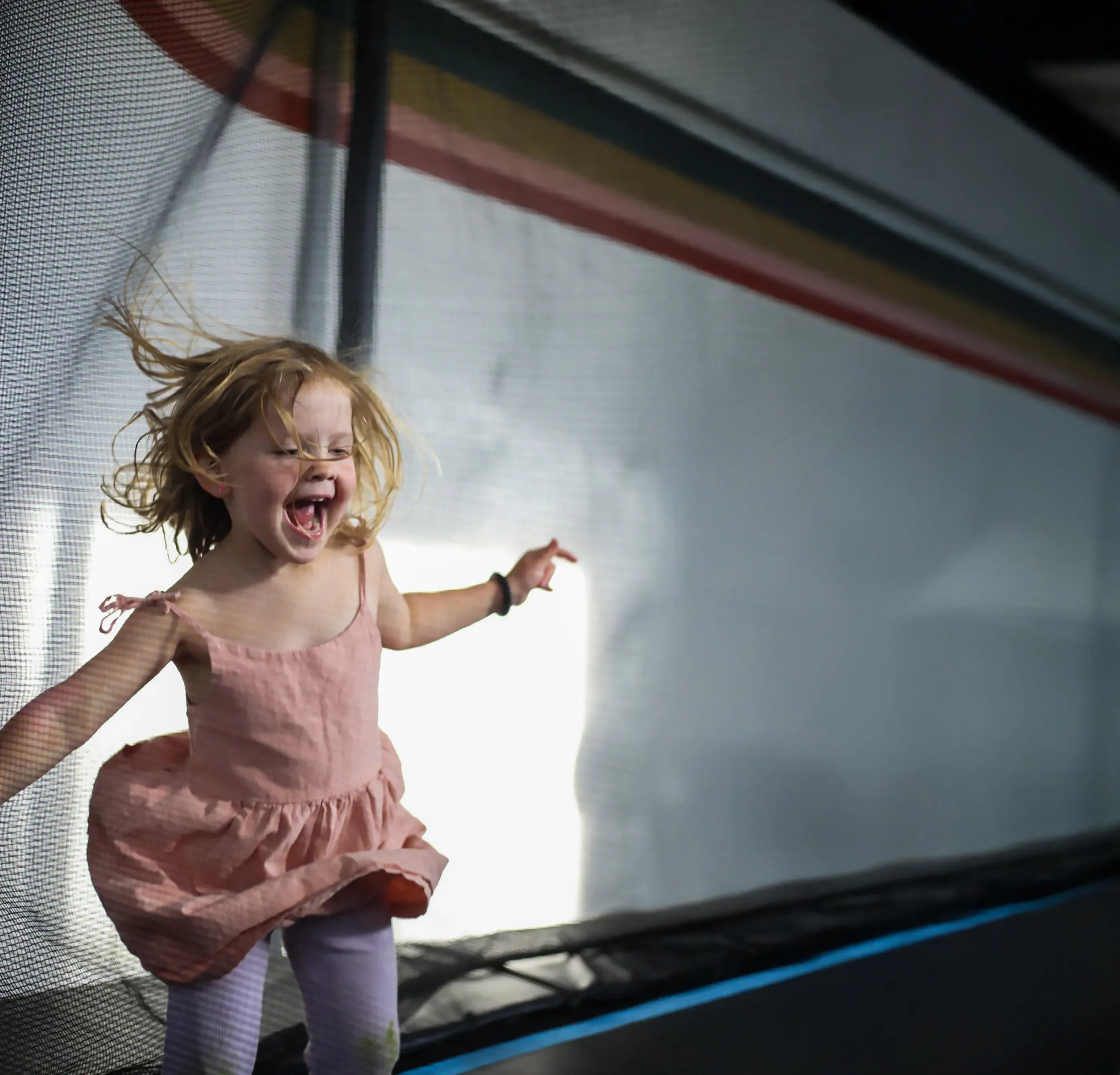 Child in a pink dress on an Acon trampoline laughing with joy.