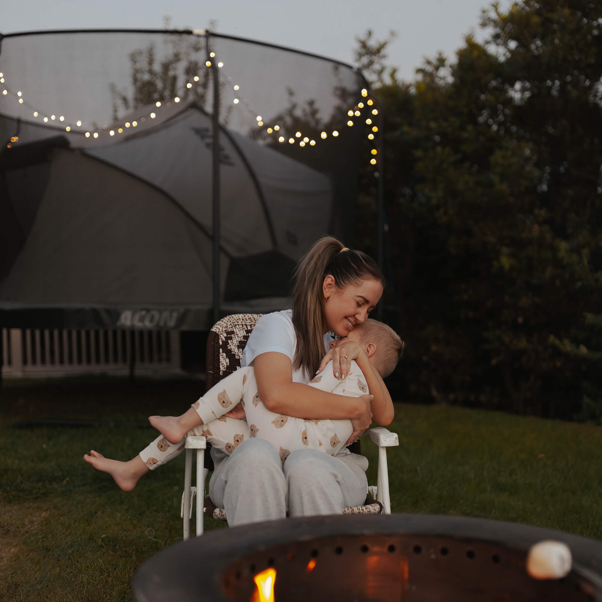 Mother hugging her child, Acon Trampoline decorated with lights in the background, an Acon Trampoline Tent on it.