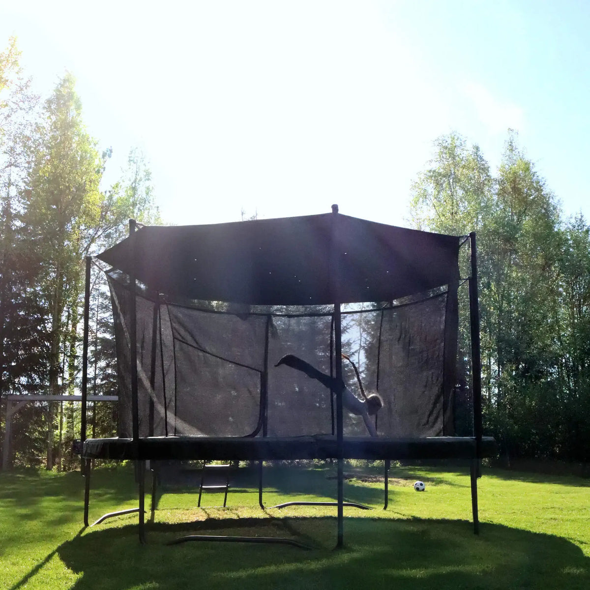Child playing on an ACON trampoline with a Sun Shade in a sunny backyard.