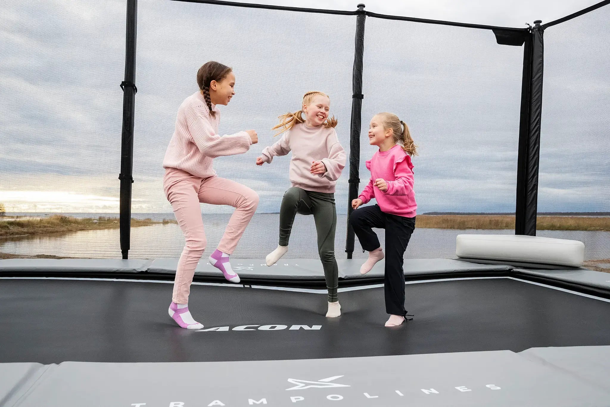 Three girls jumping and playing on a Acon trampoline, smiling and having fun.