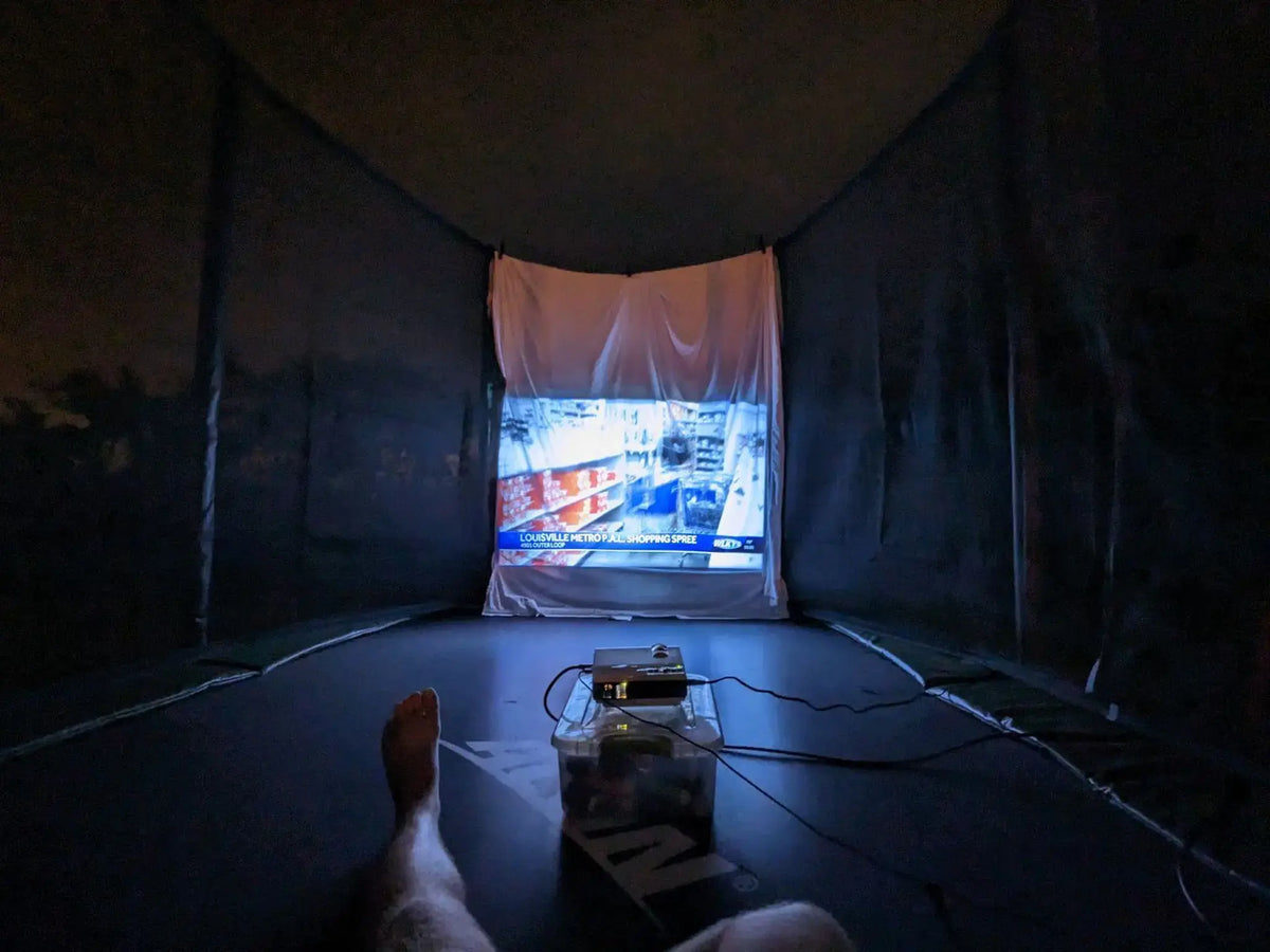 Projector displaying a movie on a white screen inside an Acon trampoline enclosure.
