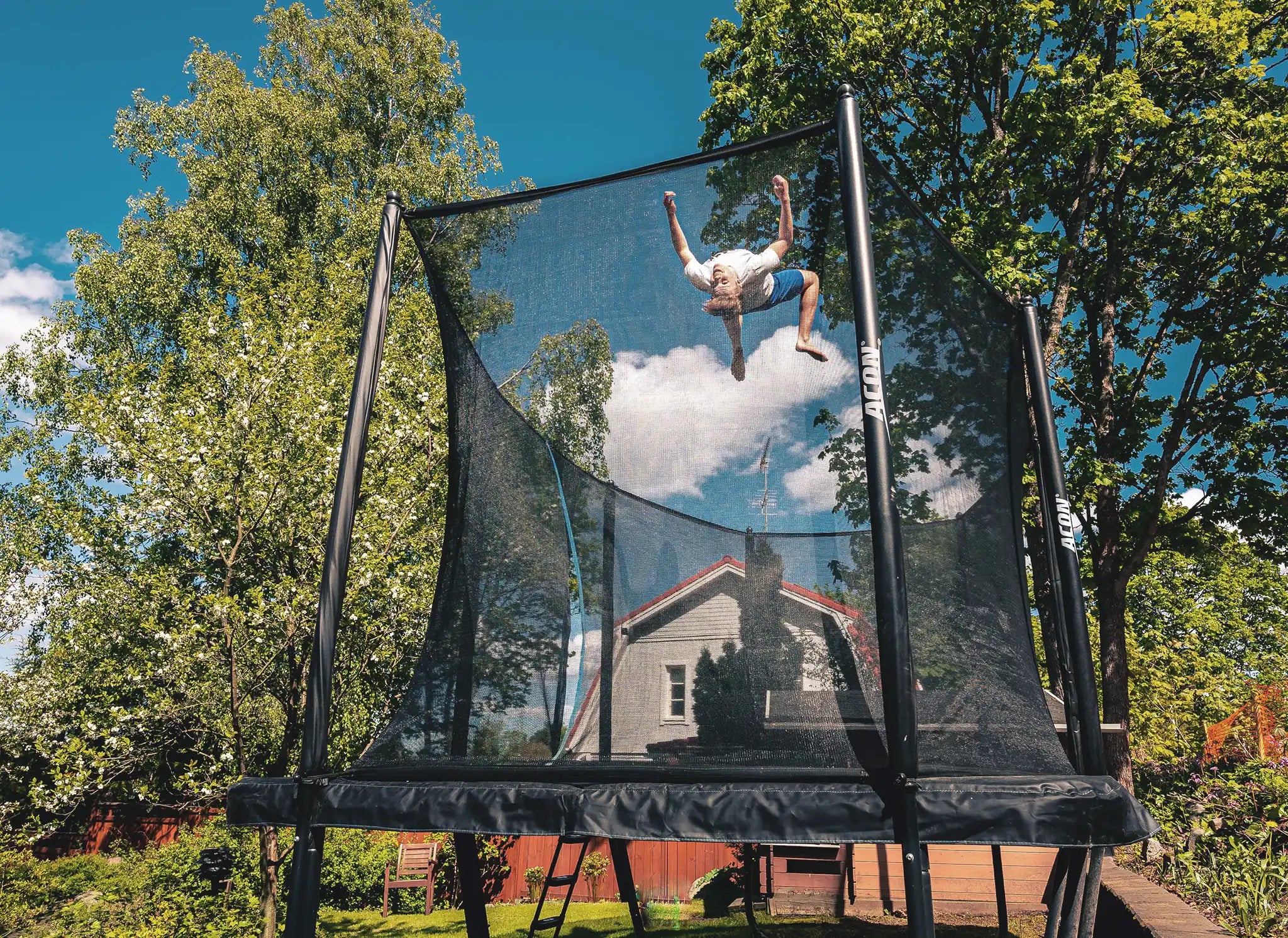 A young guy doing a flip on a rectangular trampoline with net.