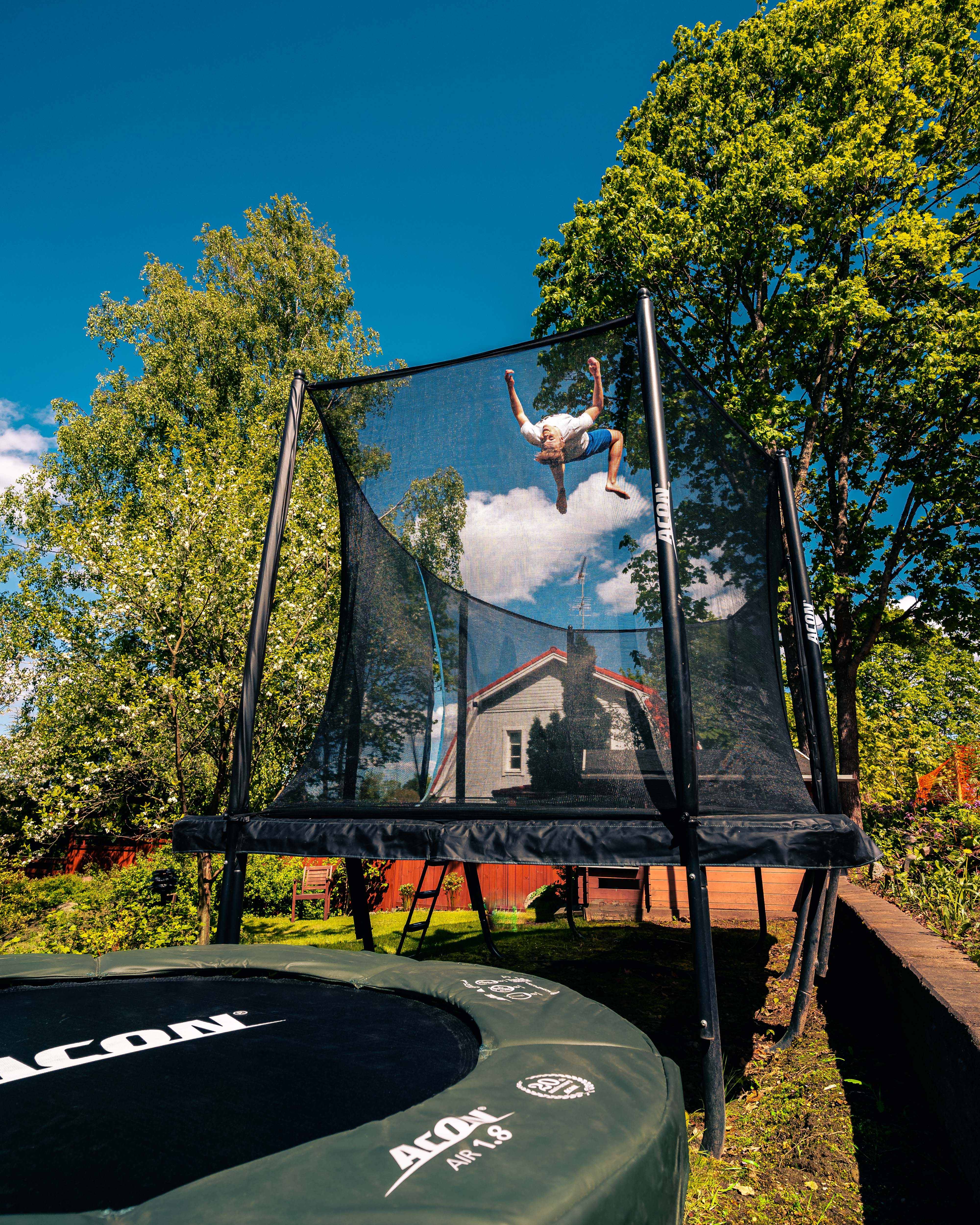 A young guy doing a flip on a rectangular trampoline with net