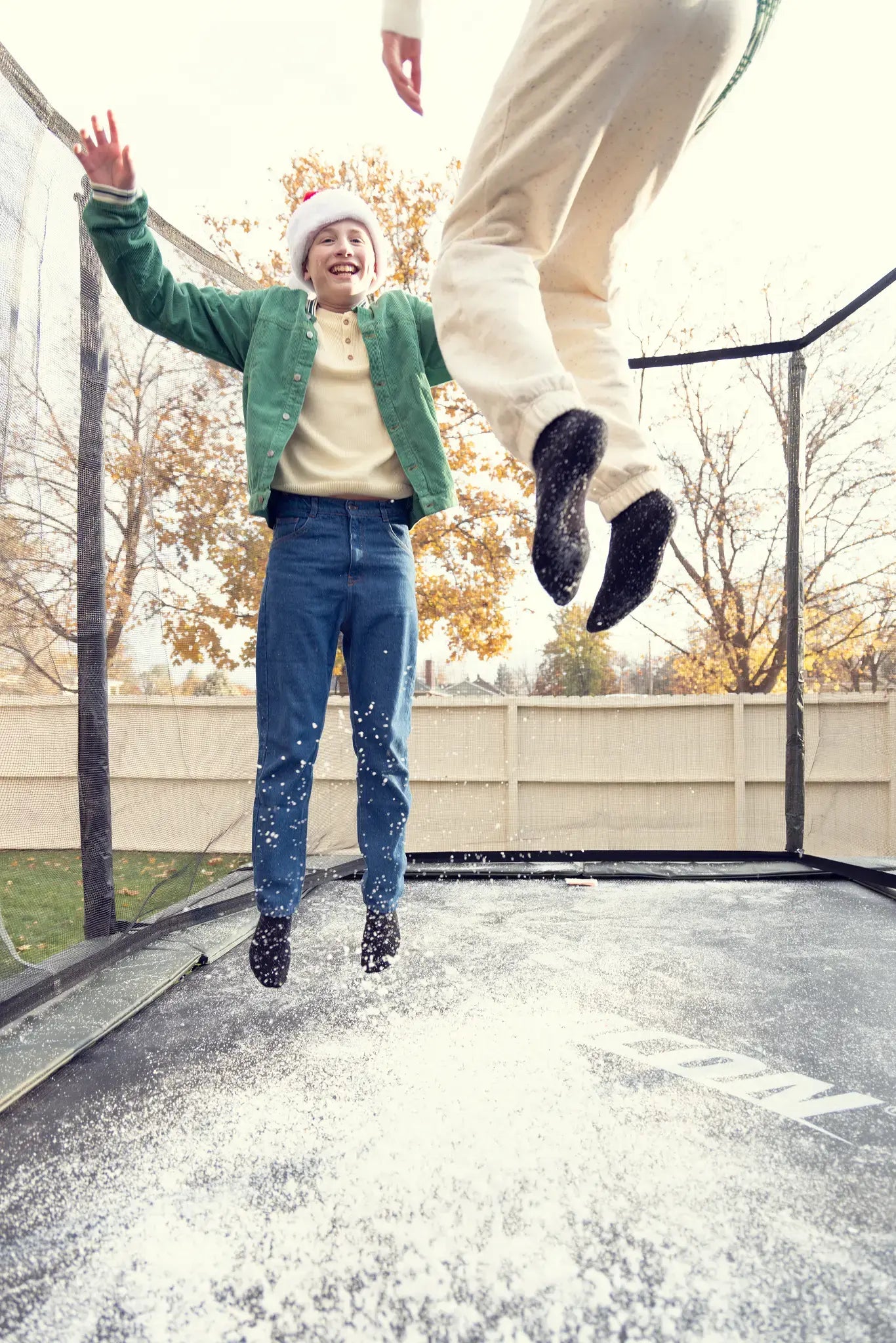 Two kids bouncing on a snowy Acon trampoline in winter clothes, one wearing a Santa hat and smiling.