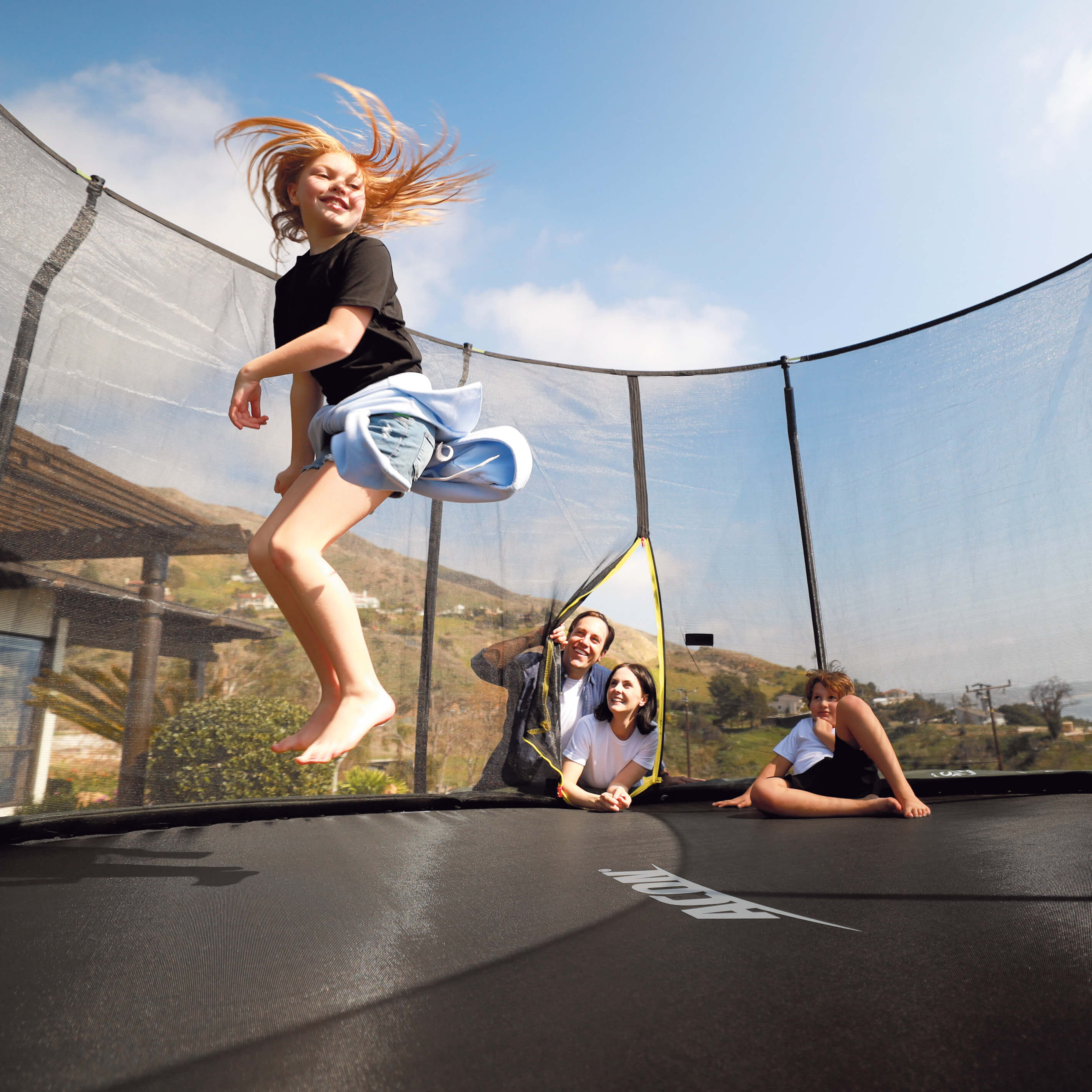 Girl jumps on an Acon trampoline, family watches.