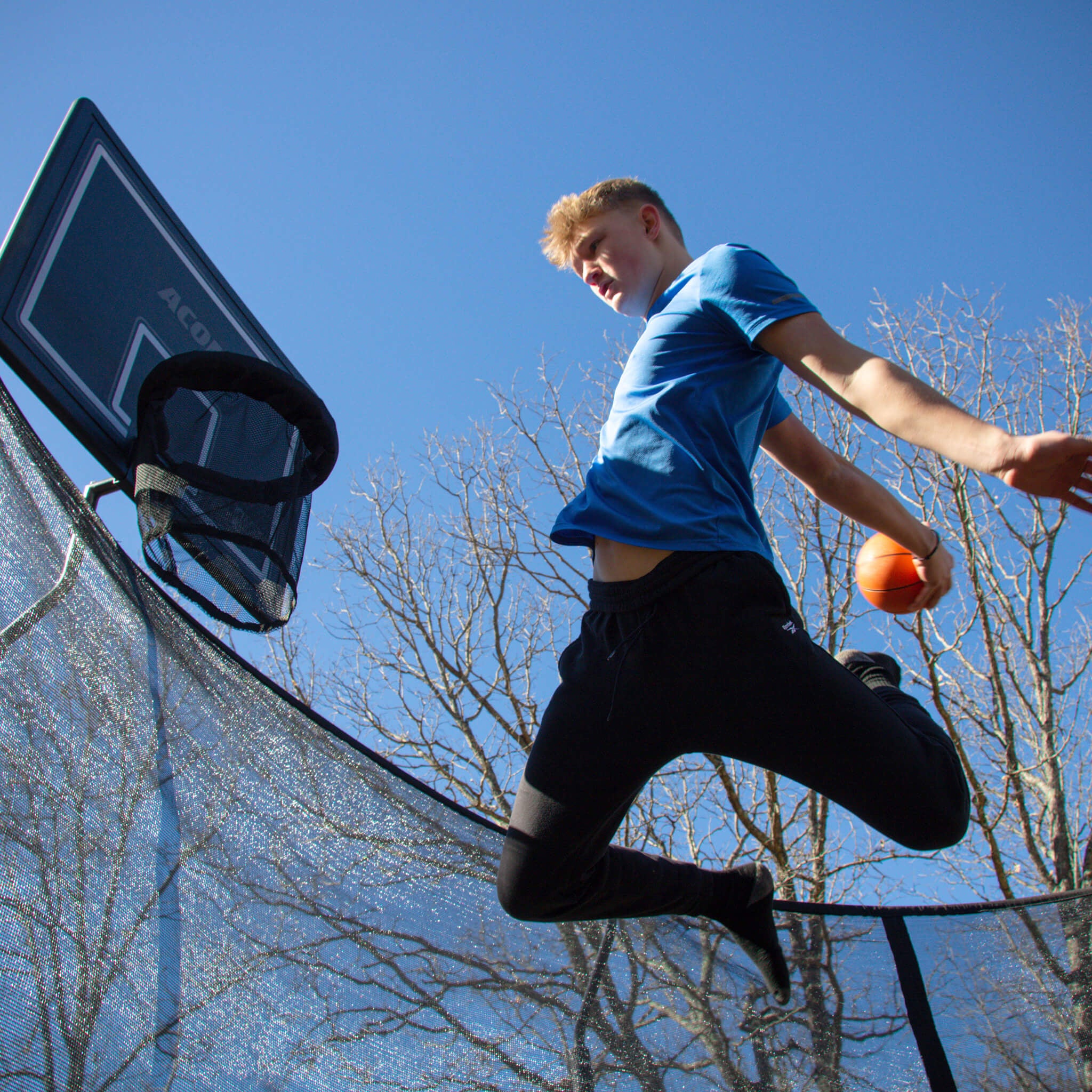 A boy plays trampoline basketball.